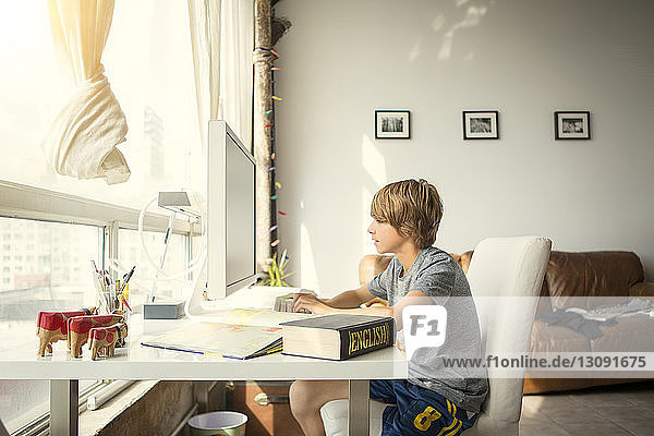 Seitenansicht eines Jungen  der einen Desktop-Computer benutzt  während er am Tisch sitzt