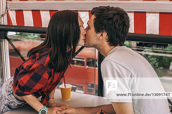 Seitenansicht eines jungen Paares  das sich im Café auf den Mund küsst