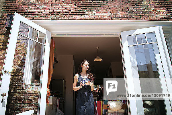 Smiling woman standing on doorway during sunny day