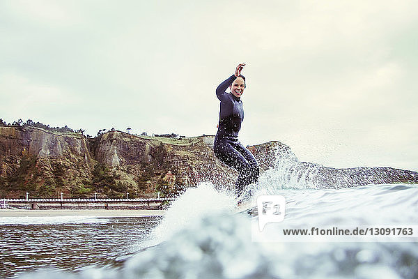 Portrait of happy woman surfing on sea against cloudy sky
