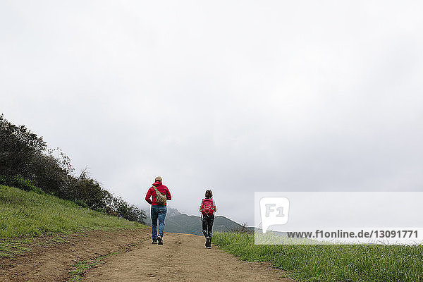 Rear view of father and daughter walking on walkway against sky