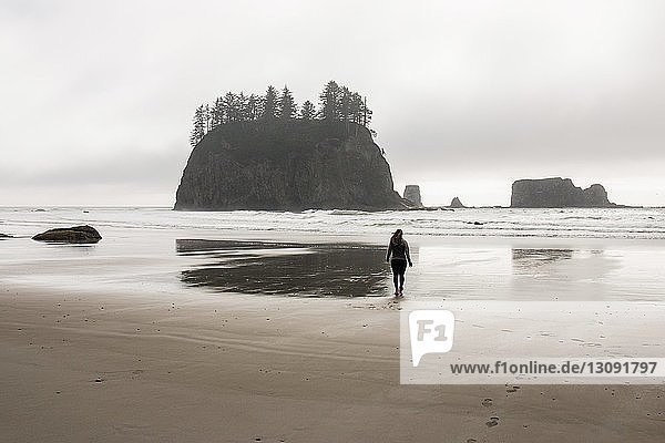 Rear view of woman standing at beach against cloudy sky in Olympic National Park