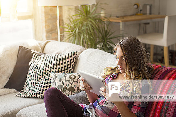 High angle view of girl using tablet computer while sitting on sofa at home