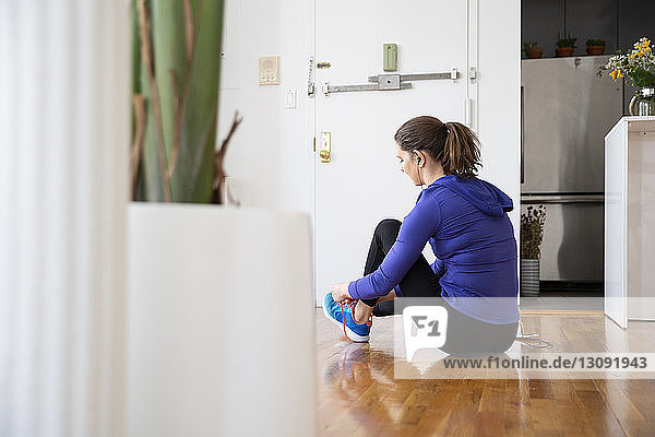 Seitenansicht einer Frau beim Schnürsenkelbinden  während sie zu Hause auf dem Boden sitzt