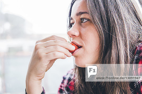 Nahaufnahme einer nachdenklichen Frau  die in einem Café am Fenster Erdbeeren isst