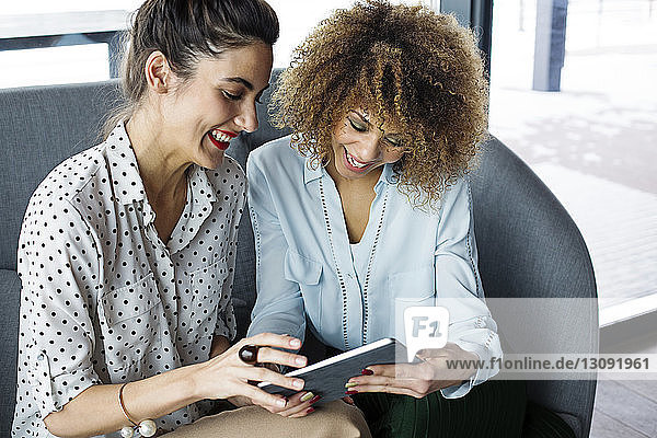 Cheerful female colleagues using tablet computer at cafe