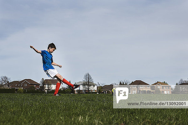 Seitenansicht eines Jungen beim Fussballspielen auf einem Rasenplatz gegen den Himmel