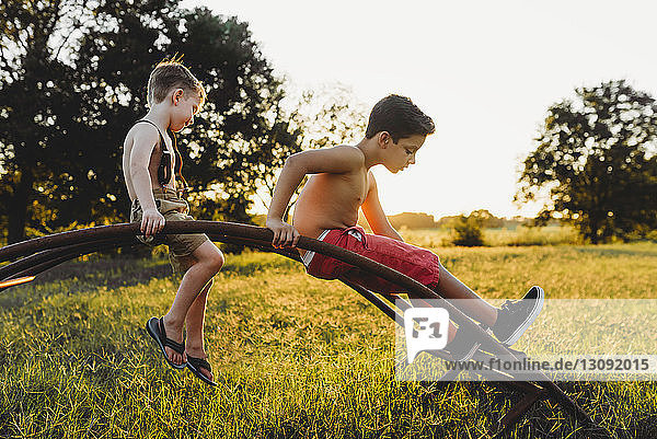 Brüder ohne Hemd spielen bei Sonnenuntergang auf einer Metallstruktur auf dem Spielfeld