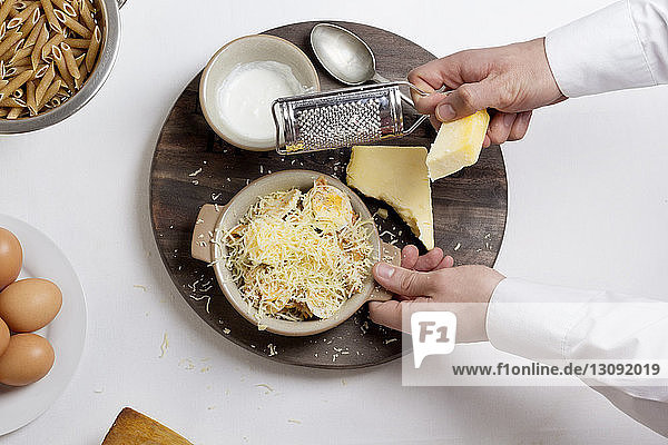 Draufsicht des Küchenchefs  der Käse auf gekochten Eiern in einer Schüssel reibt