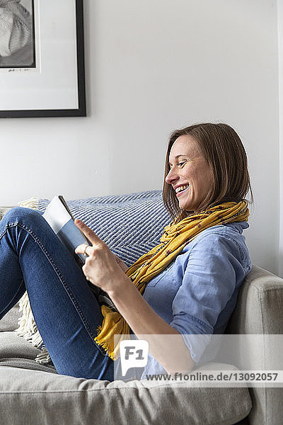 Glückliche Frau liest Zeitschrift  während sie zu Hause auf dem Sofa sitzt