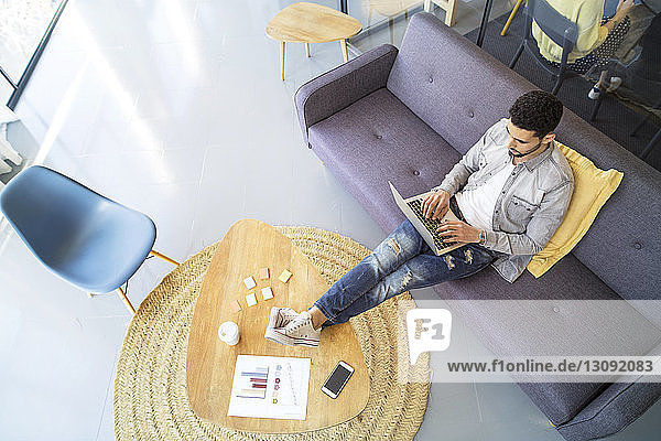 Hochwinkelansicht eines Geschäftsmannes mit Laptop-Computer  während er im Büro auf dem Sofa sitzt