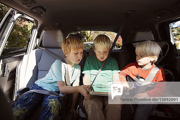 Brüder schauen auf Tablet-Computer  während sie im Auto sitzen