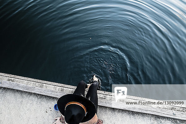 Schrägansicht einer Frau mit Filzhut  die am Pier am Meer sitzt