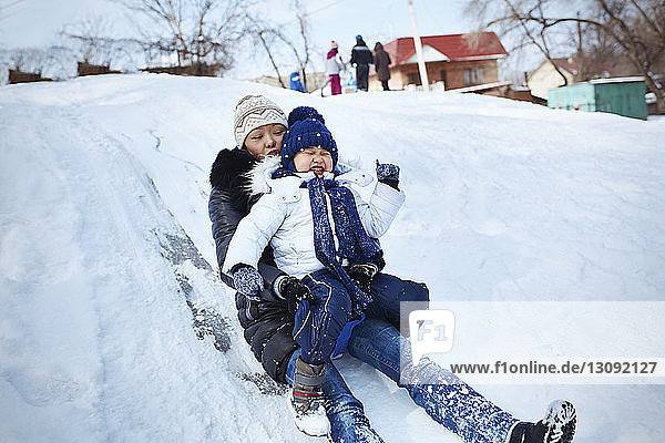 Mother and daughter tobogganing on snowy field