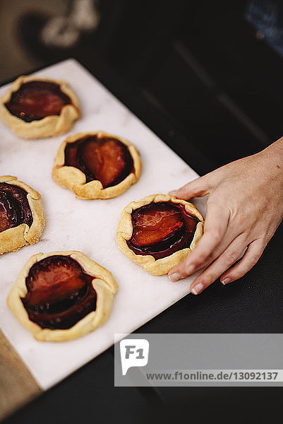 High angle view of woman taking rustic plum tart from serving tray