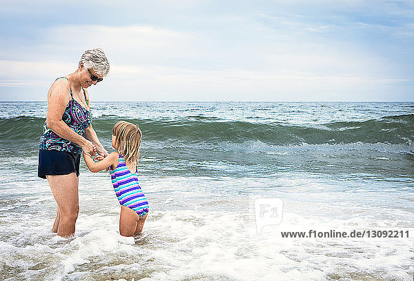 Verspielte Großmutter mit im Wasser stehender Enkelin am Strand