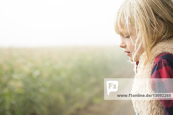 Seitenansicht eines Mädchens  das weg schaut  während es bei Pflanzen gegen den Himmel steht