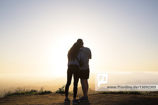 Rear view of couple standing on mountain against clear sky during sunset
