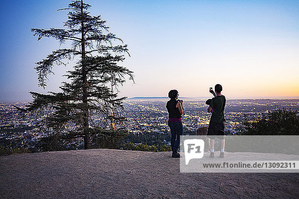 Silhouette von zwei Personen  die in der Abenddämmerung im Griffith Park Fotos vom Stadtbild machen