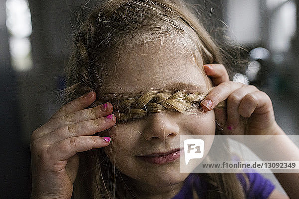 Close-up of girl covering eyes with braided hair at home