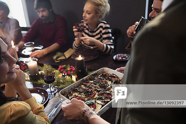 Woman serving food to happy friends at table during Christmas party