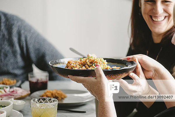 Glückliche Frau reicht Reisteller an Freundin weiter  während sie am Tisch sitzt