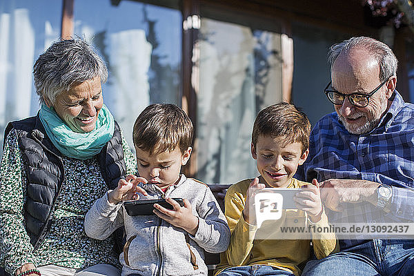 Glückliche Großeltern sehen Enkel an  die im Park Smartphones benutzen