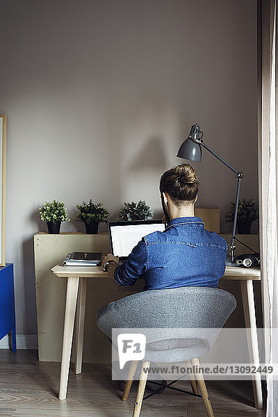 Rear view of man using laptop computer while sitting at table