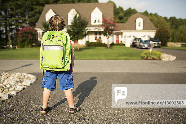 Rear view of schoolboy with backpack standing on street during sunny day