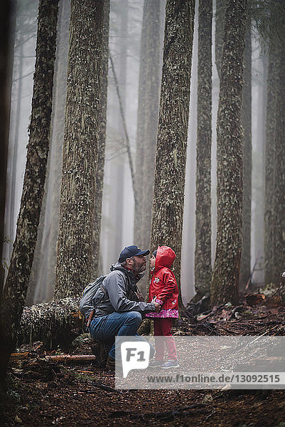 Father kissing daughter while crouching in forest