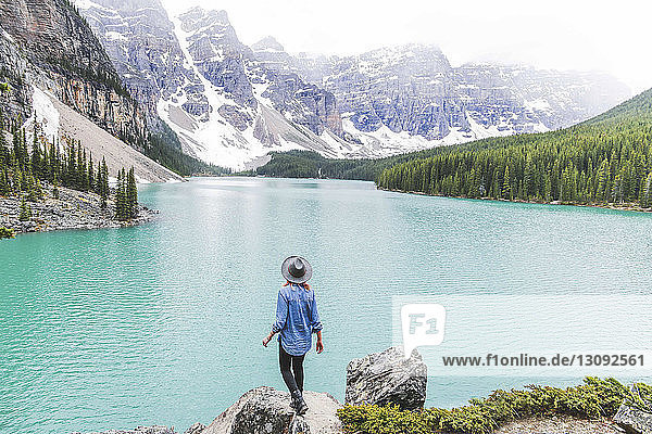 Rear view of woman in fedora hat standing on rock by Moraine Lake against mountains