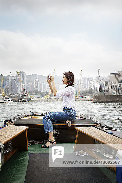 Side view of female tourist photographing while sitting on boat in city