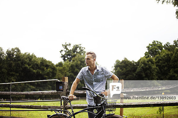 Mann steht mit dem Fahrrad auf dem Bauernhof vor klarem Himmel