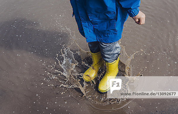 Low section of playful boy wearing yellow rubber boots while splashing puddle
