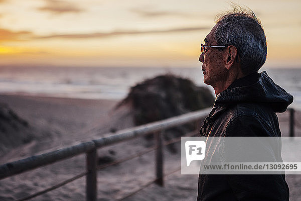 Thoughtful senior man standing at beach during sunset