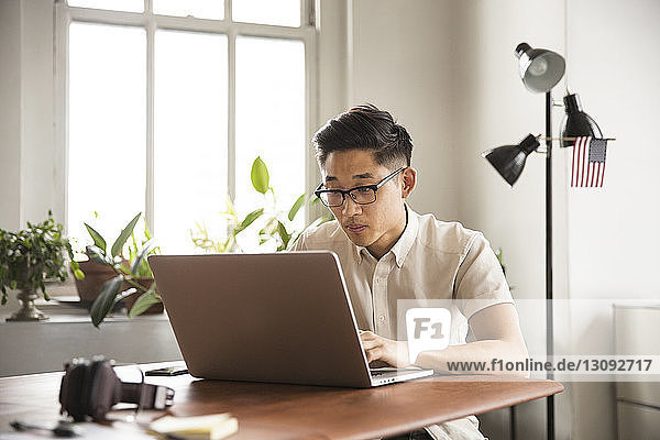 Seriöser Geschäftsmann benutzt Laptop  während er im Kreativbüro am Tisch sitzt