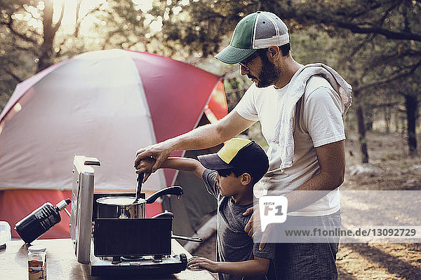 Vater und Sohn bereiten im Wald auf einem Campingkocher Essen zu