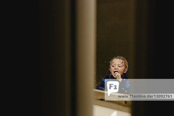 Junge beim Zähneputzen reflektiert auf Spiegel durch Türöffnung gesehen