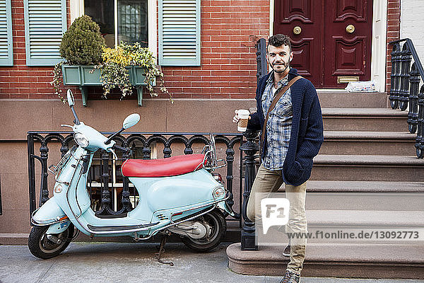 Porträt eines Mannes  der sich mit einem Motorroller an einem Geländer gegen ein Gebäude in der Stadt lehnt
