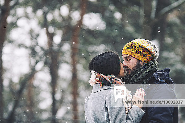 Romantic couple kissing while standing in forest during winter