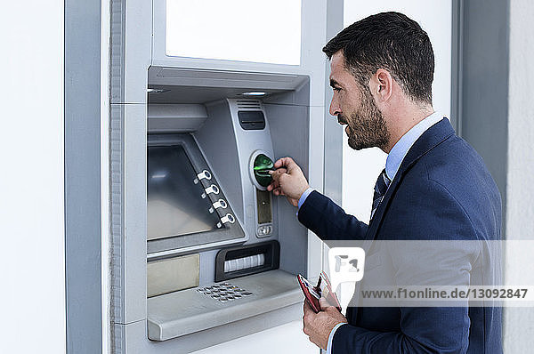 Seitenansicht eines Geschäftsmannes  der an der U-Bahn-Station einen Geldautomaten benutzt
