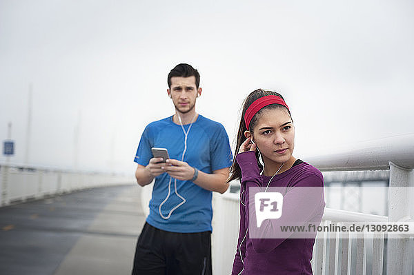 Selbstbewusste Sportlerin trägt Kopfhörer  während sie mit einem Freund auf der Bay Bridge steht