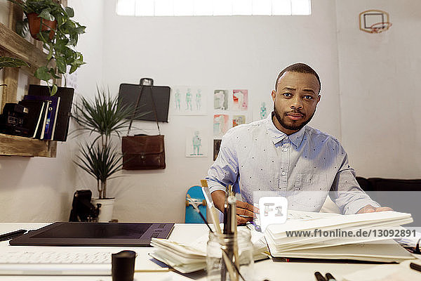 Porträt eines selbstbewussten Illustrators  der im Kreativbüro am Schreibtisch sitzt