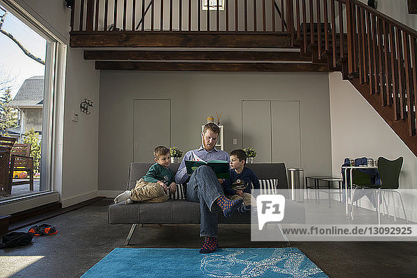 Vater zeigt Söhnen Buch  während er zu Hause auf dem Sofa sitzt