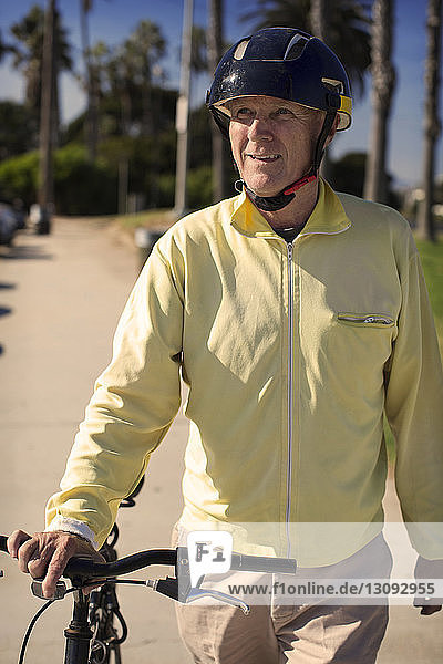Smiling man looking away while standing with bicycle in park