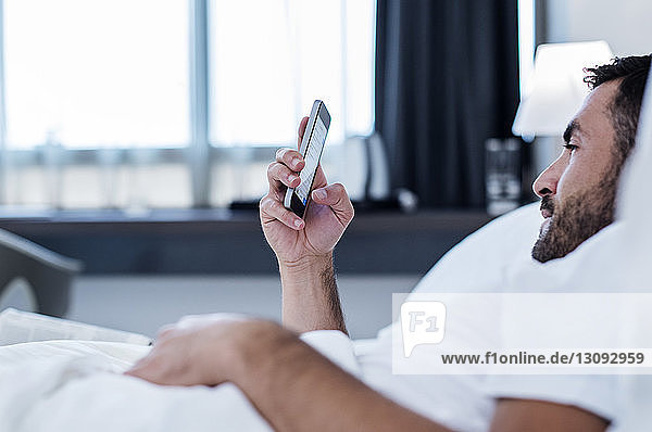 Seitenansicht eines Mannes mit einem Smartphone im Hotelzimmer