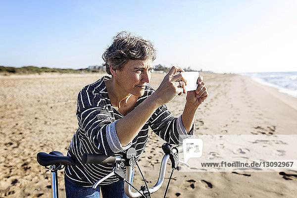 Woman photographing while standing with bicycle at beach