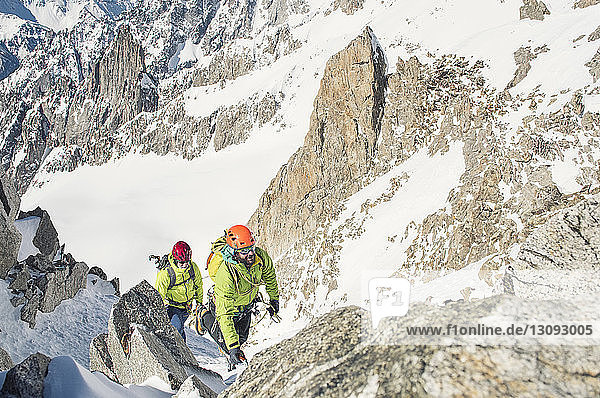 Hochwinkelaufnahme von männlichen Wanderern  die im Winter an einem sonnigen Tag den Berg besteigen