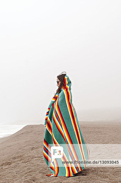 Seitenansicht einer in ein Handtuch gehüllten Frau  die auf Sand vor klarem Himmel steht
