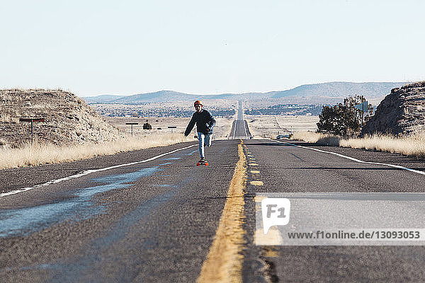 Full length of man skateboarding on road amidst field against clear sky